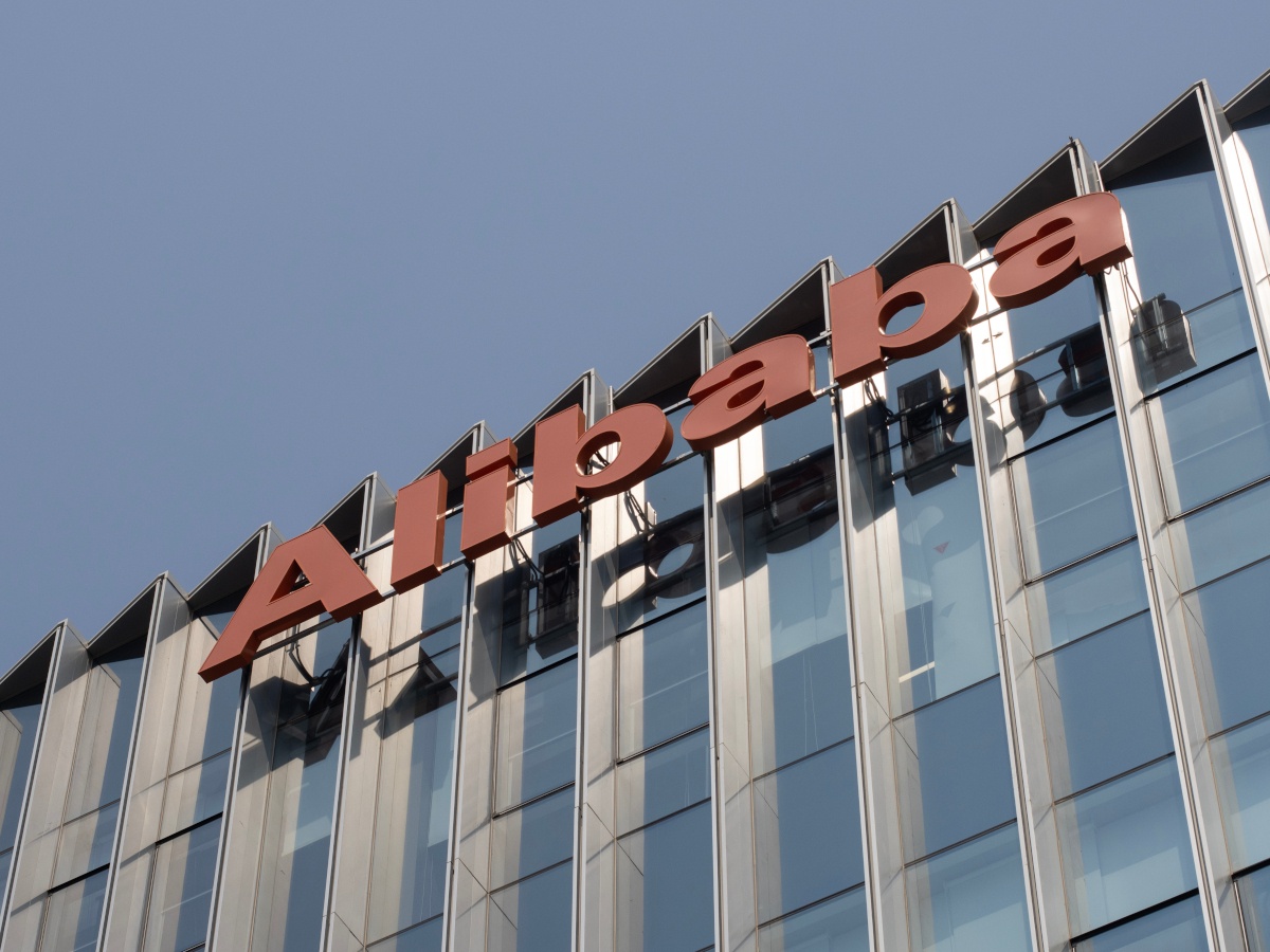 The front of a glass building, viewed at an angle, with the Alibaba logo visible.