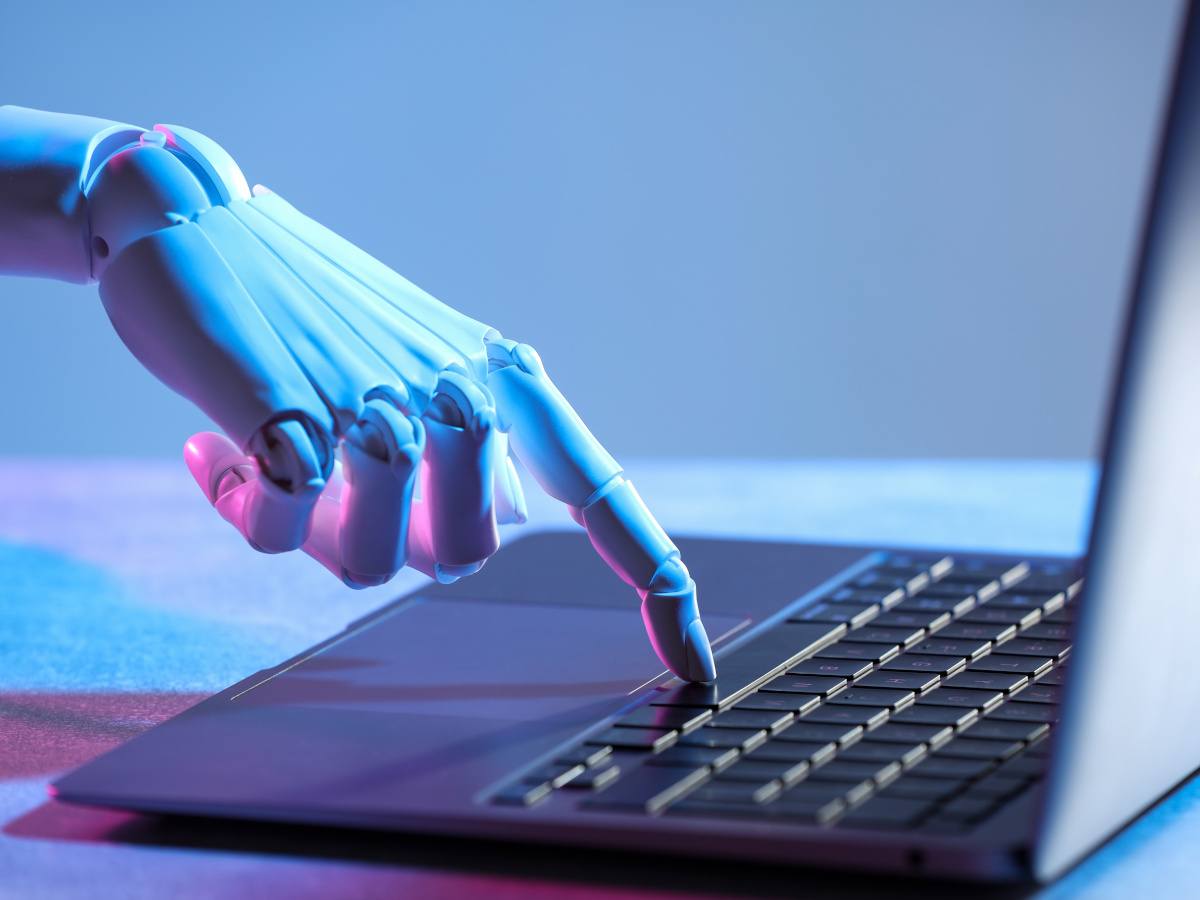 A robot hand touching a laptop keyboard.