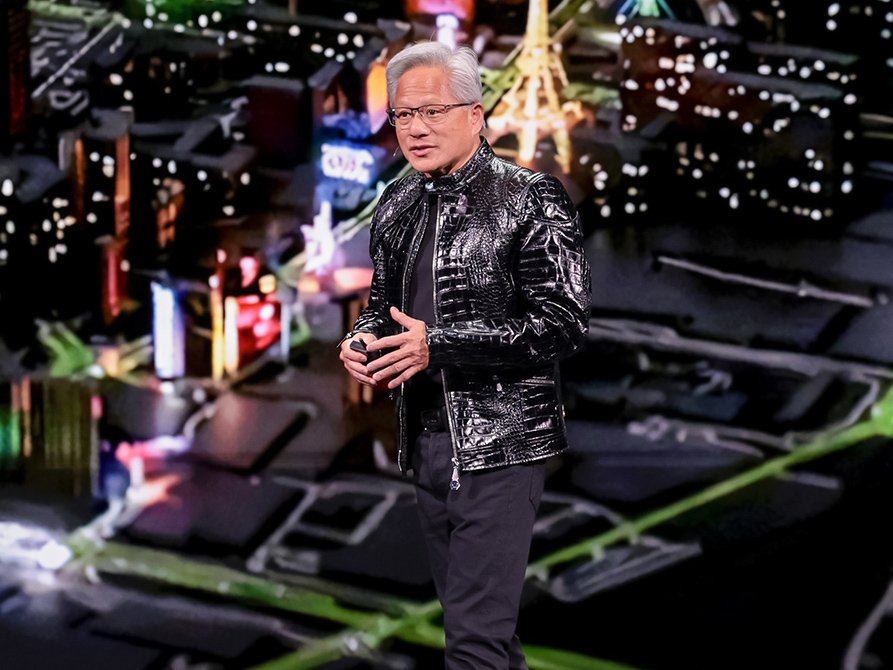 Nvidia CEO Jensen Huang in a black leather jacket with grey hair on a stage with a vivid background.