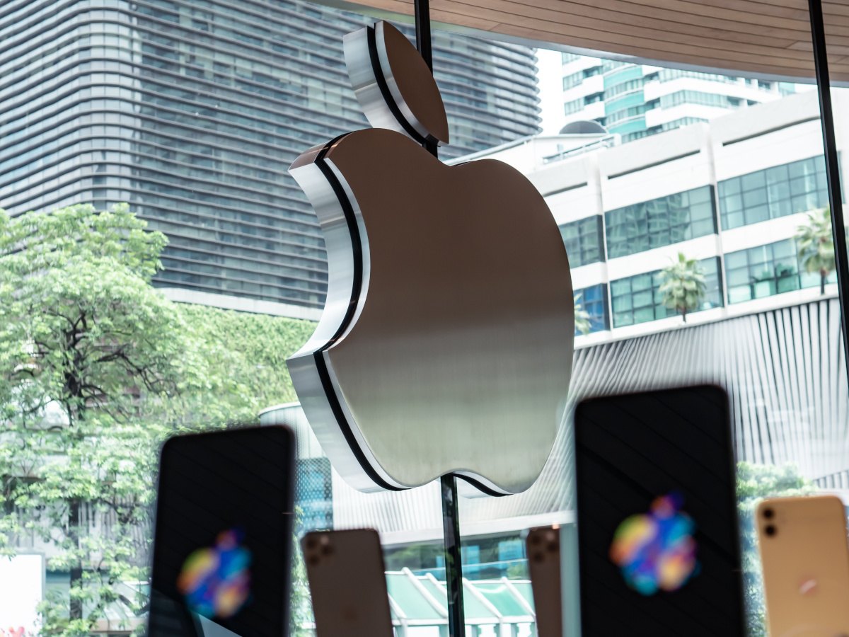 Apple company logo from inside an Apple store with iPhones showcased.