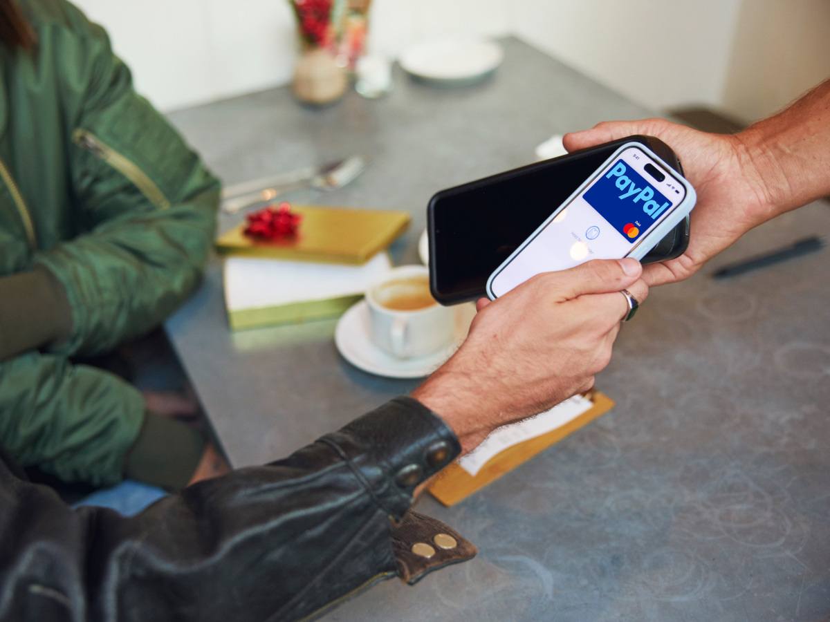 A person using their phone to tap and pay using a Paypal card.