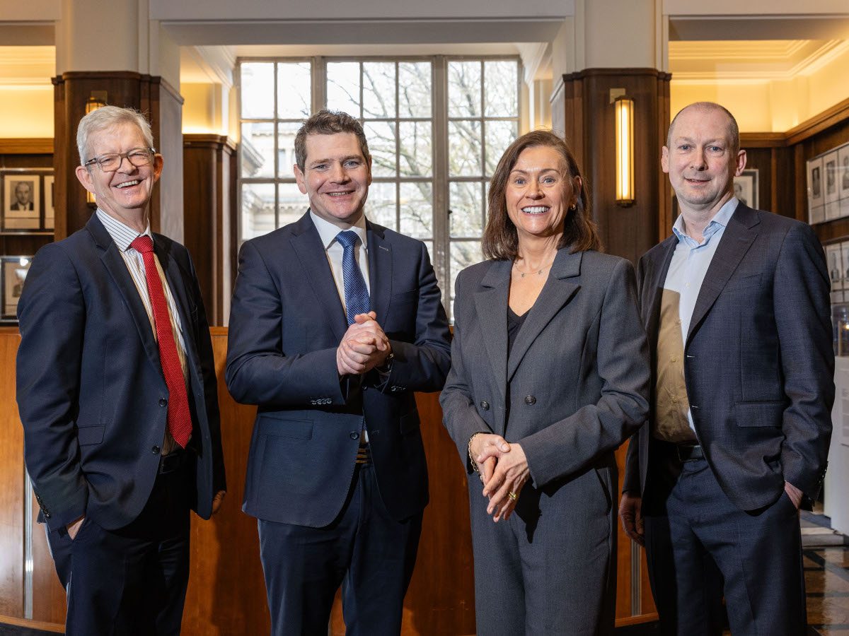 Four people wearing suits smiling.