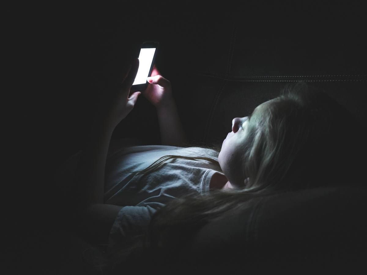 A child lying in a dark room scrolling through their phone.