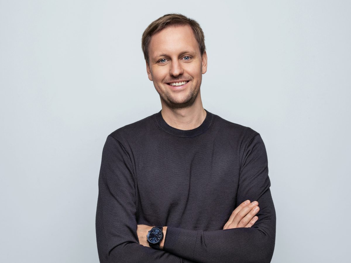 Caucasian male in long sleeved dark tee arms folded.