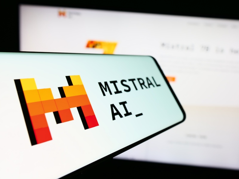 The Mistral AI logo on a smartphone screen with a larger screen in the background.