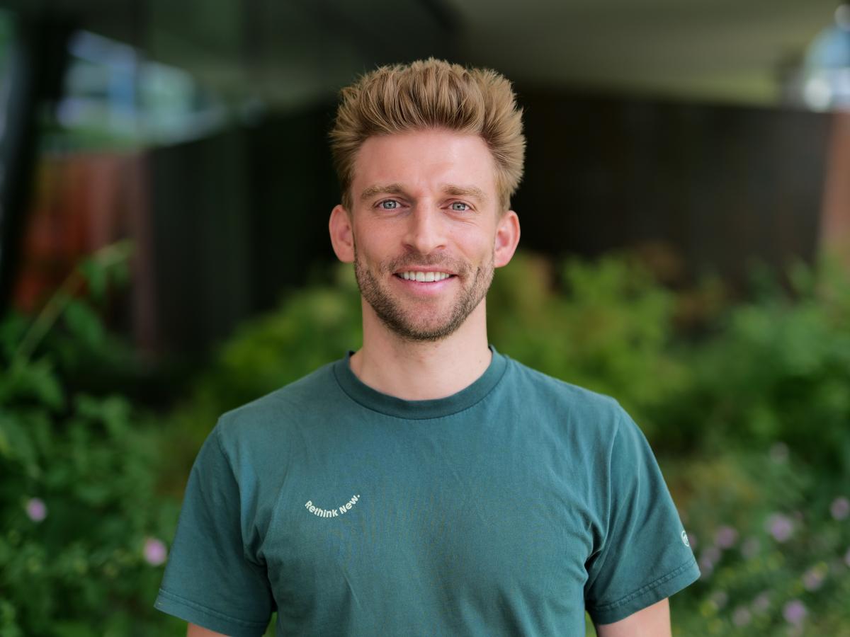 A man in a green t-shirt with light brown hair smiling at the camera.