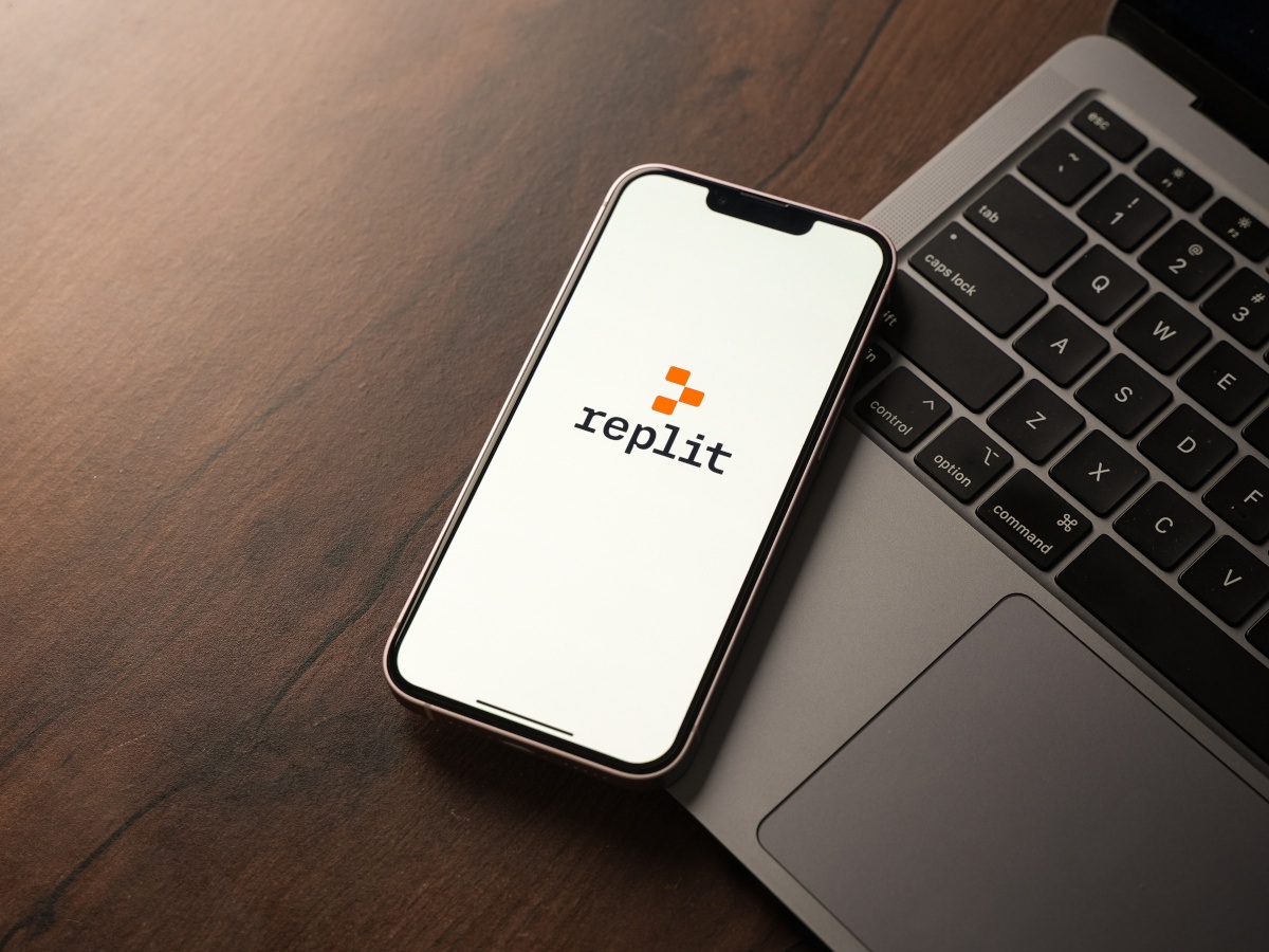 The Replit logo on a phone screen, on a device leaning against a laptop.