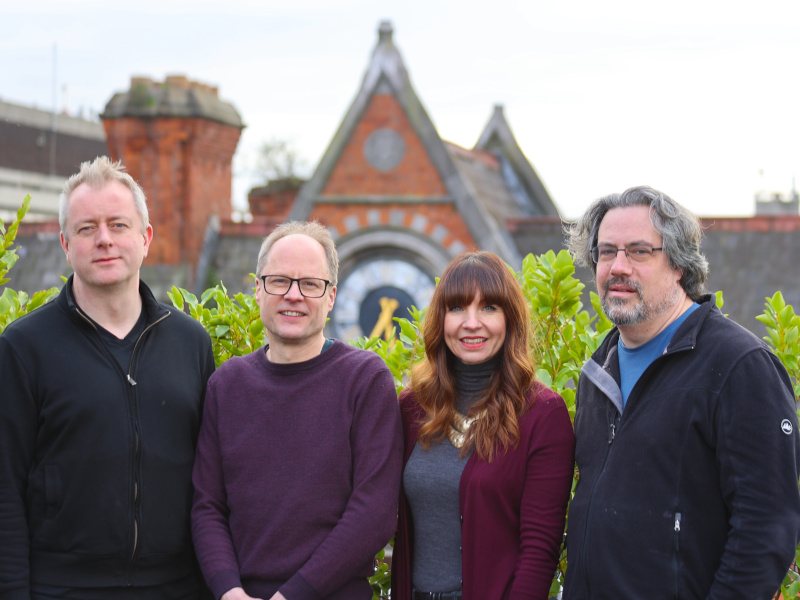 Three men and a woman stand together smiling with a pyramid shaped building in the background.