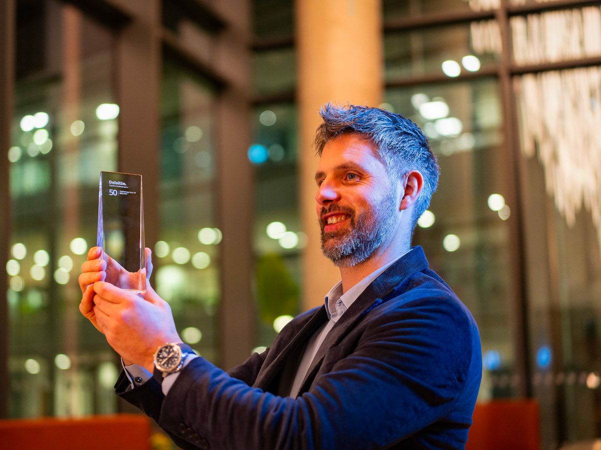 A man holding an award smiles to the side in a brightly lit room.