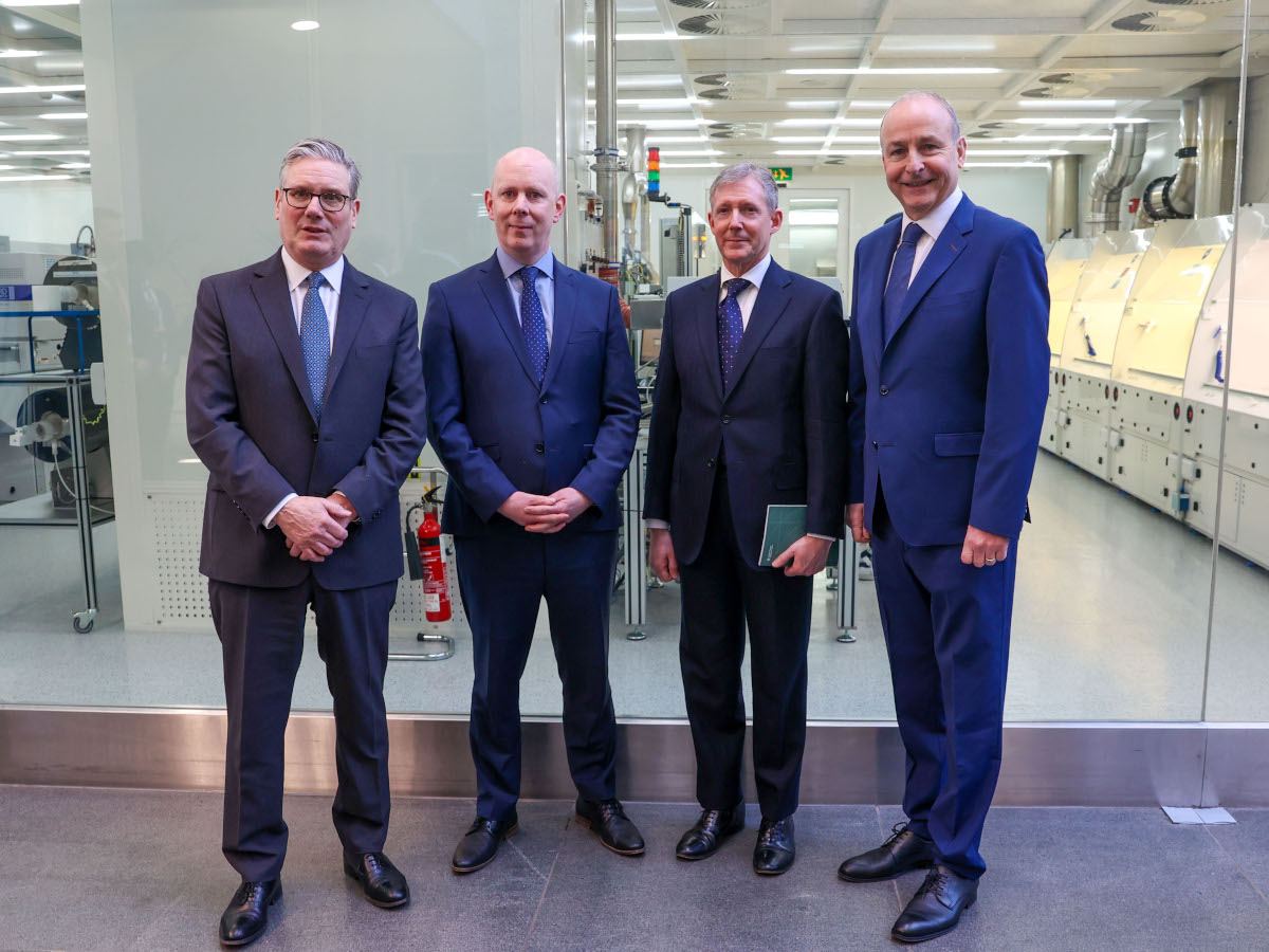 Four middle aged white men in blue and black suits pose in a lab setting.