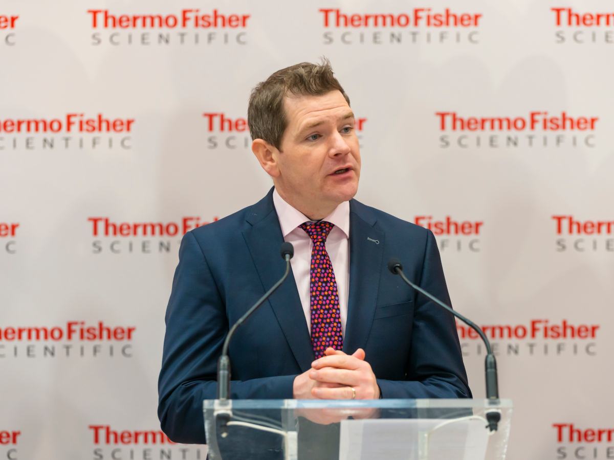 A middle-aged white man in a blue suit and red tie, standing at a podium in front of the Thermo Fisher logo.