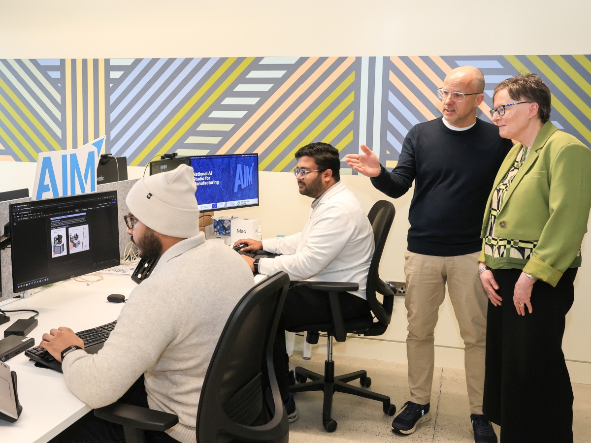 Two brown skinned men, a white man and a white woman in a tech-based office.