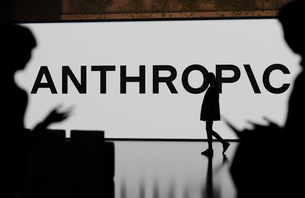 Anthropic logo on large screen, figures silhouetted in front