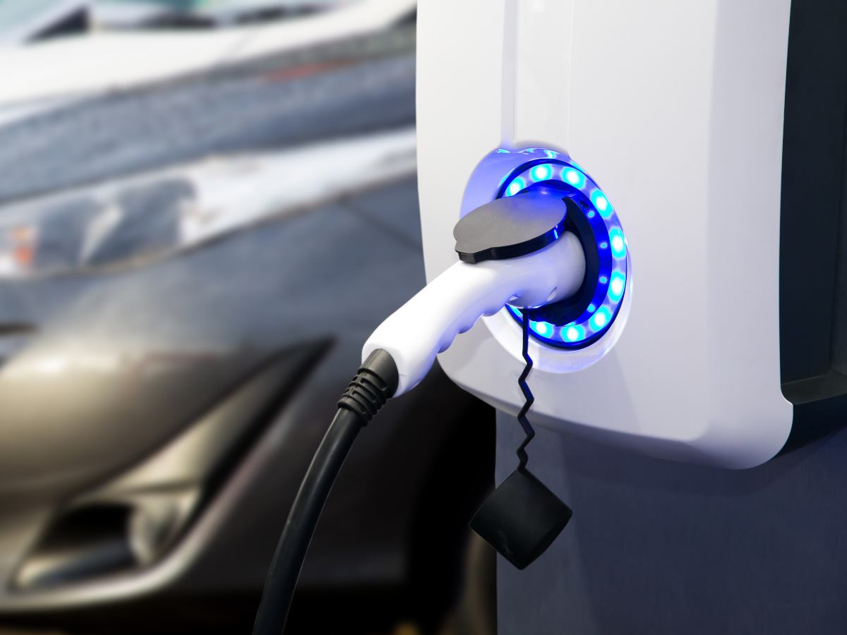 An electric vehicle charger with a car plugged into it. The rings around the charger opening are lit up in a circle of blue LEDs.