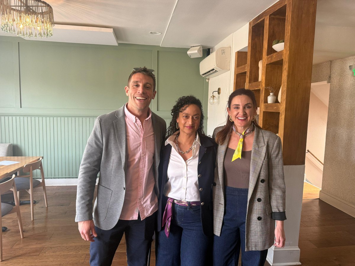 A tall man to the left is standing next to two women. All three are posing for a photograph.