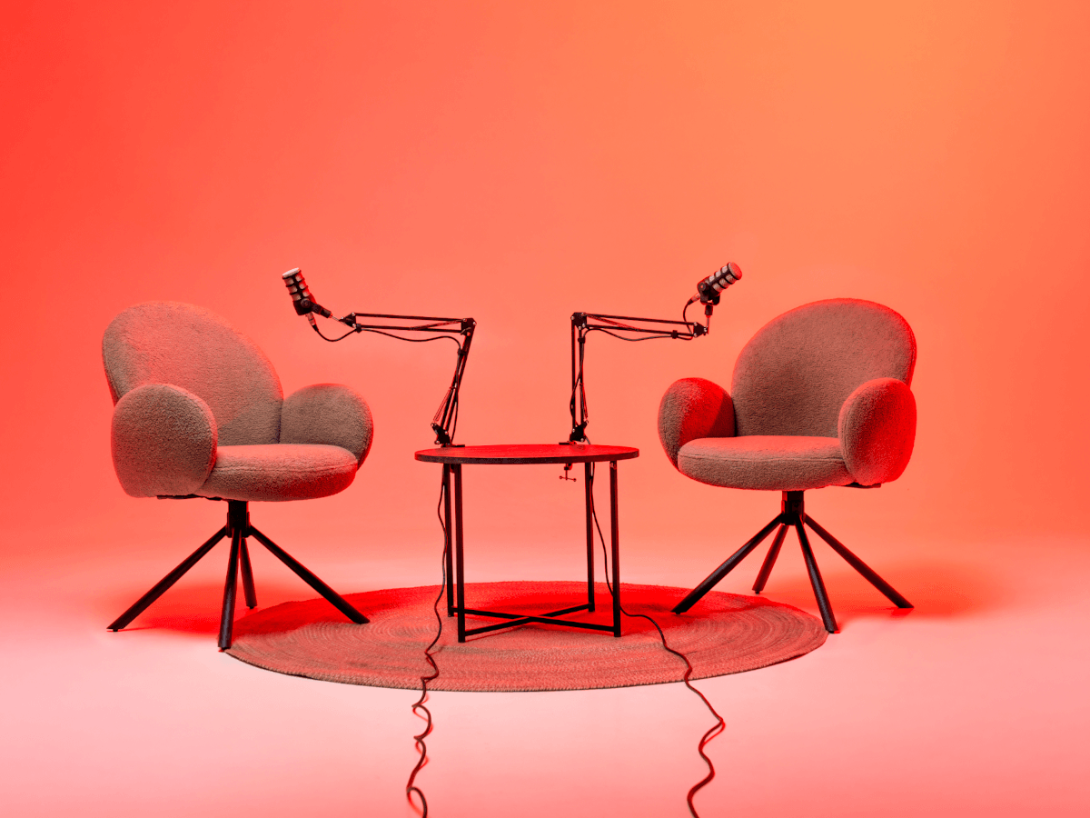 Two chairs next to a table and podcast mikes in an orange-lit room.