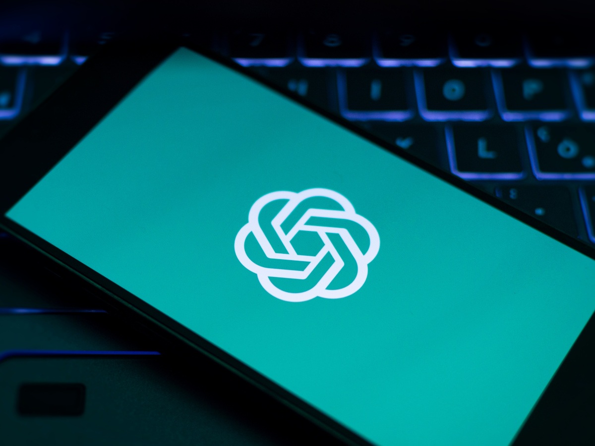 The OpenAI logo against a green background on a phone atop a laptop.