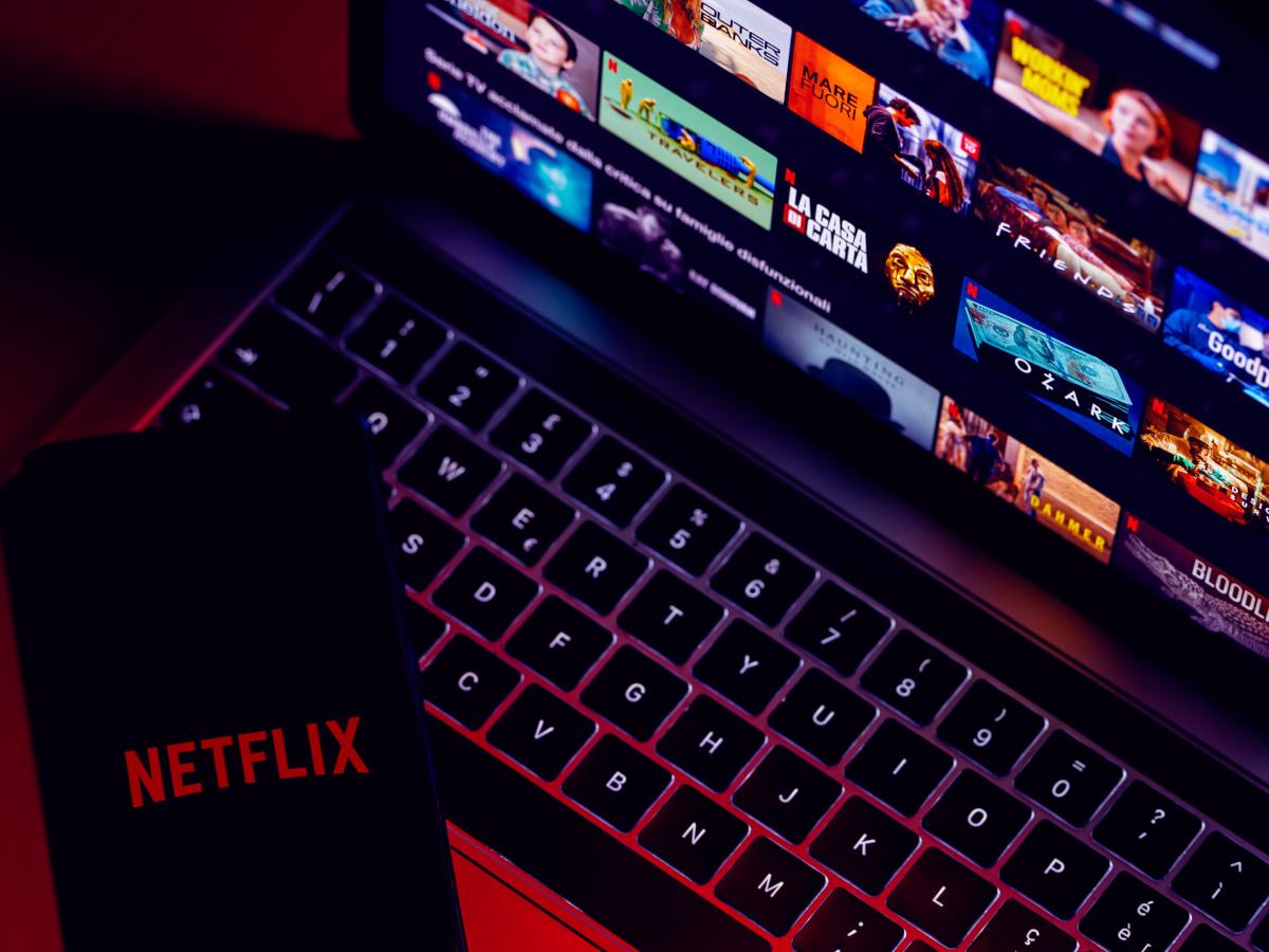 A picture of a phone screen and laptop keyboard and screen displaying the Netflix homepage.
