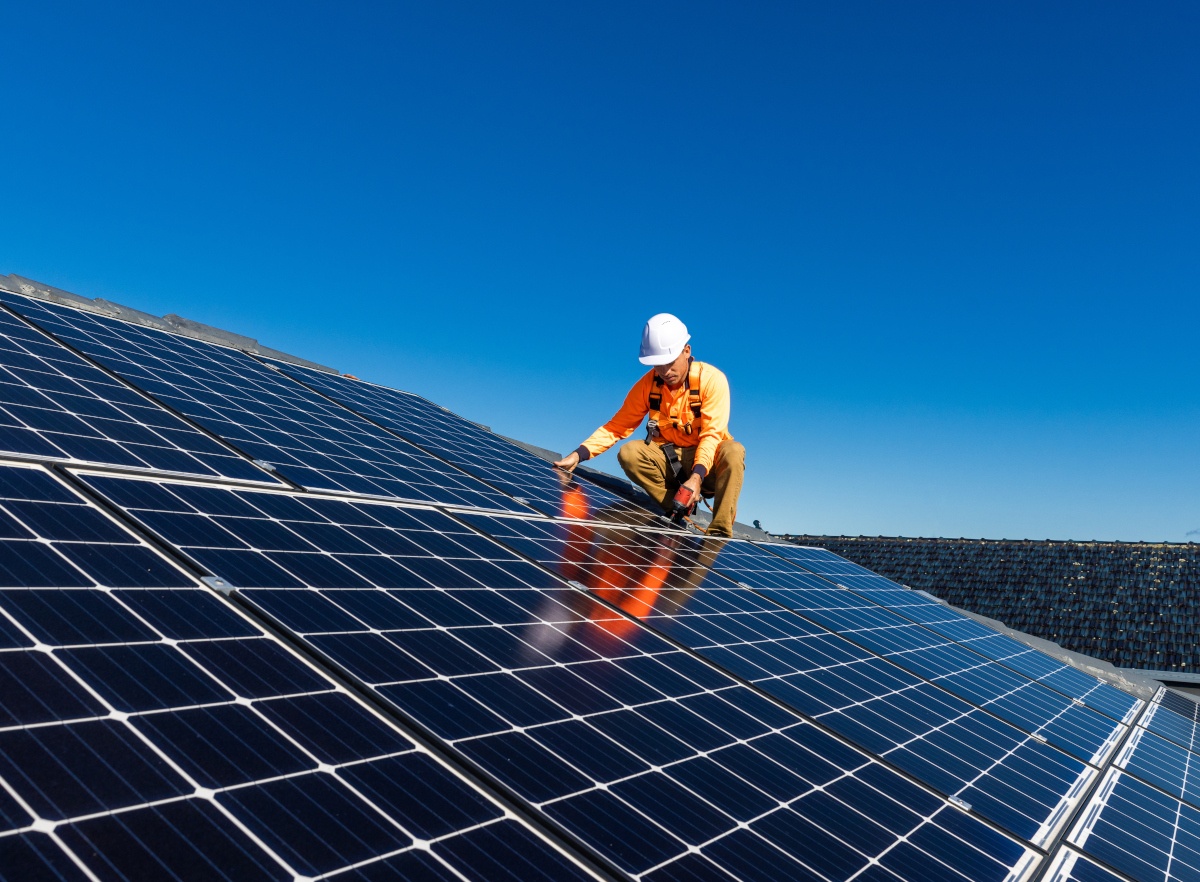 Man with hard hat installing solar array on rooftop.