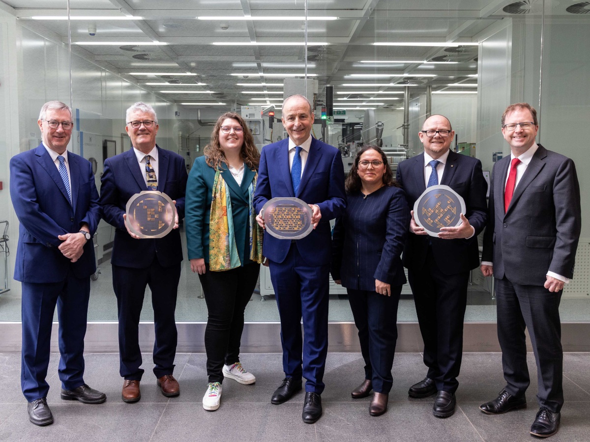 Five men and two women, all wearing business attire, stand and smile together in an office.