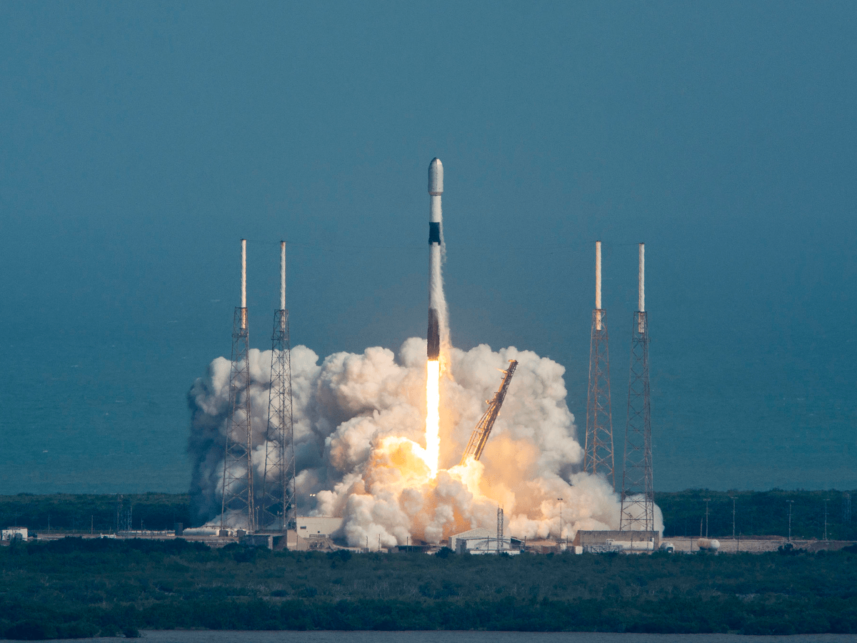 A rocket launching from afar with plumes of smoke rising underneath it.
