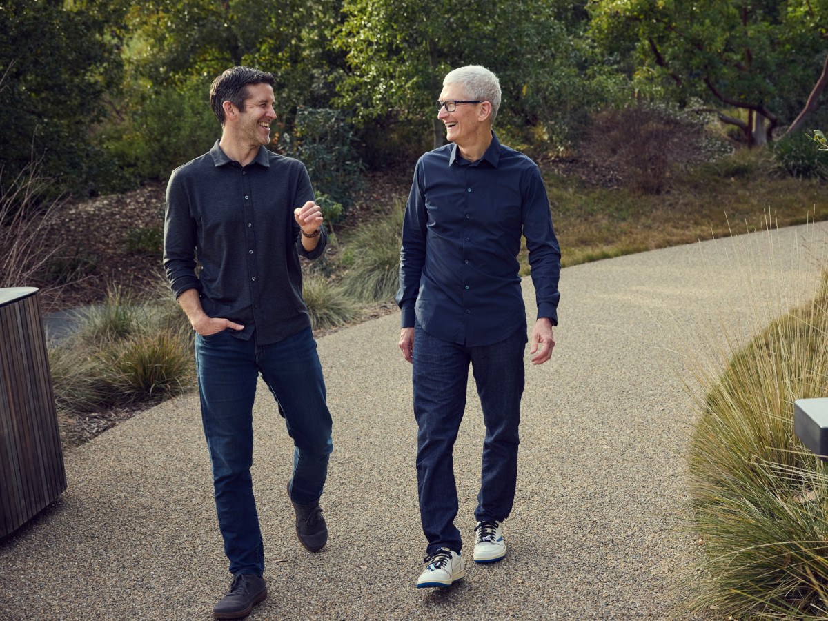 Two men in casual clothes talking down a narrow path with landscaping around.