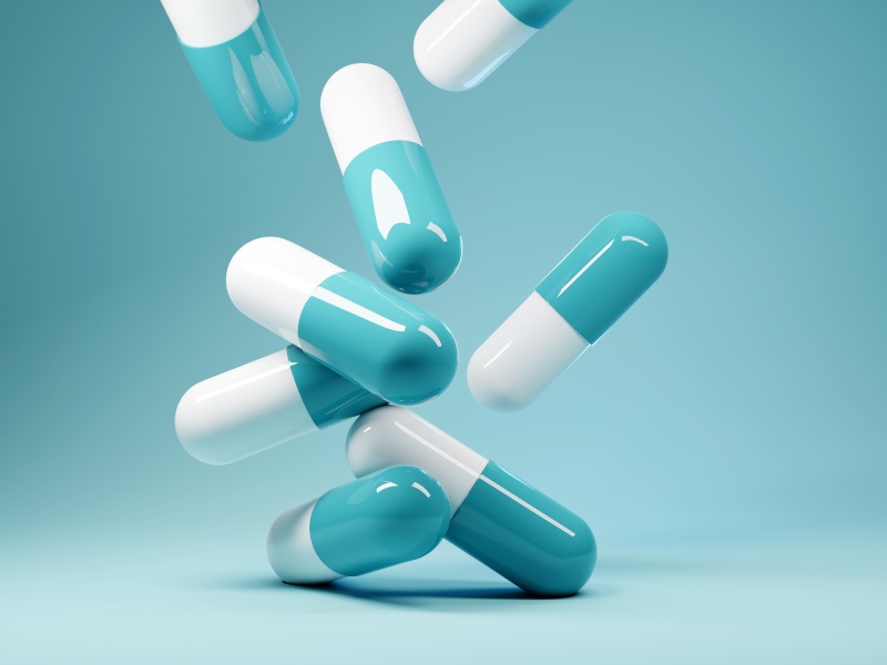Multiple pills landing on a blue surface. Used to represent antibiotics and antibiotic resistance.