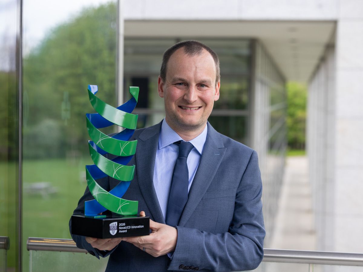 A man wearing a suit with a navy tie smiles holding a green trophy.