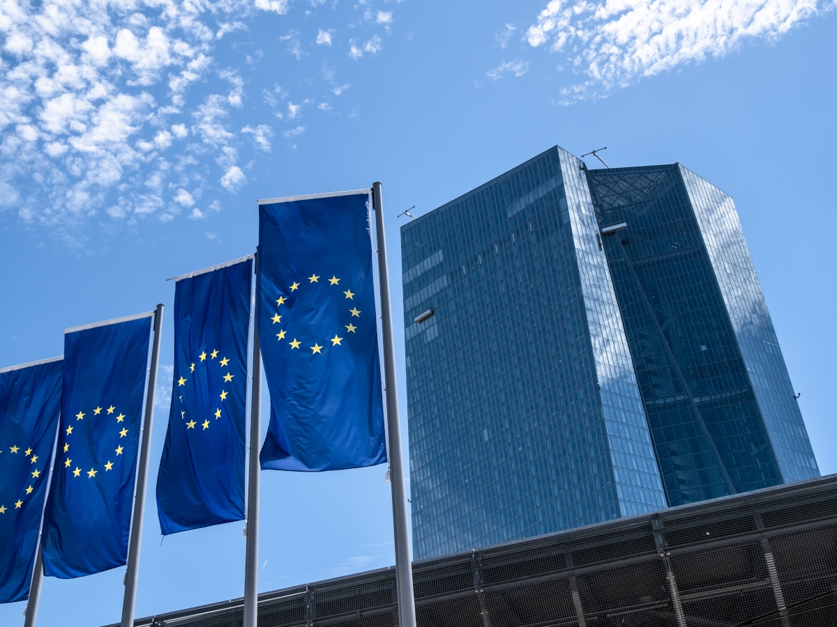 A picture of EU flags sitting outside a tall office building against a blue sky.