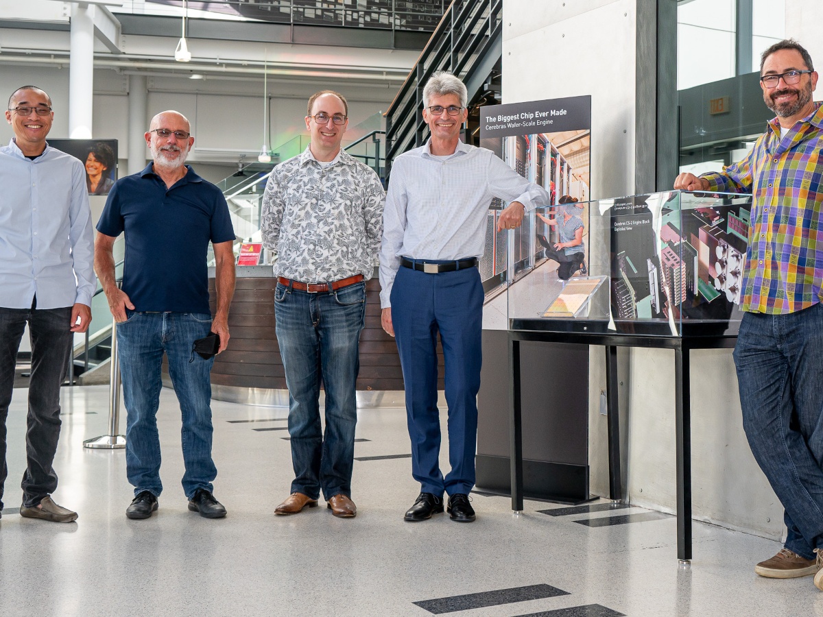 A group of men in casual wear in a brightly lit room with a Wafer Scale Engine.