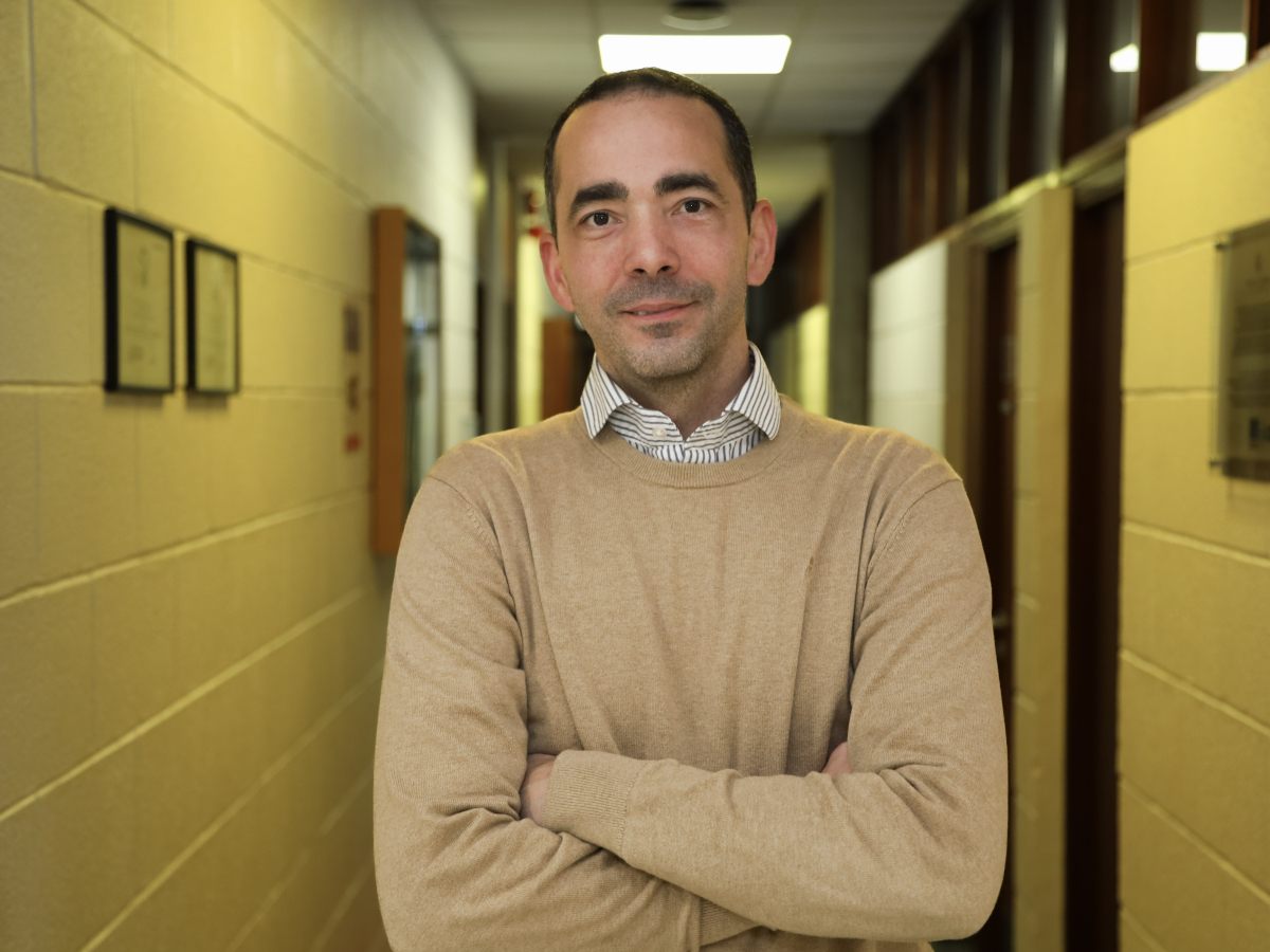 A man in smart casual wear posing with arms crossed in a hallway.