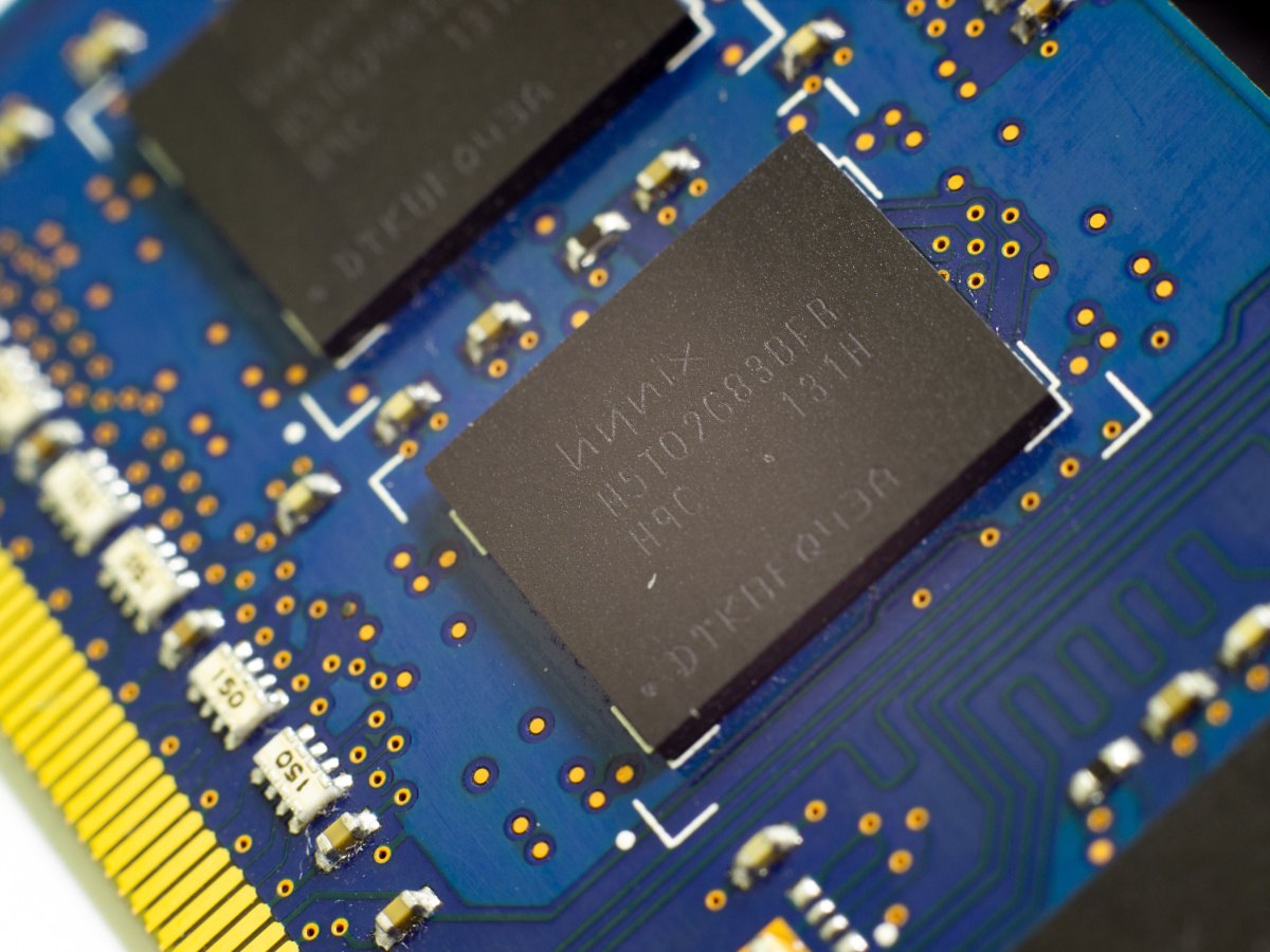 A close-up of a SK Hynix memory chip on a blue motherboard with yellow configurations seen to the left.
