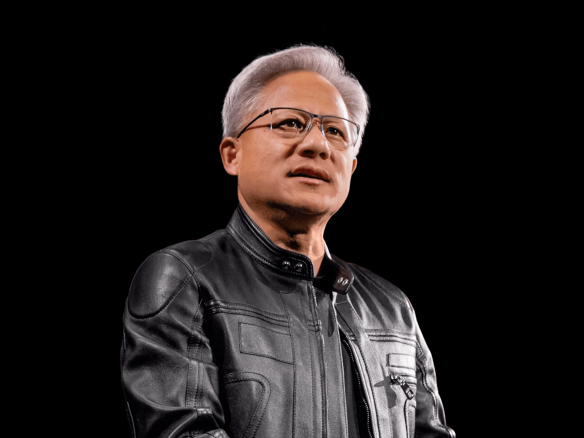 A man with grey hair and glasses in a black leather jacket. Bust shot with black background.