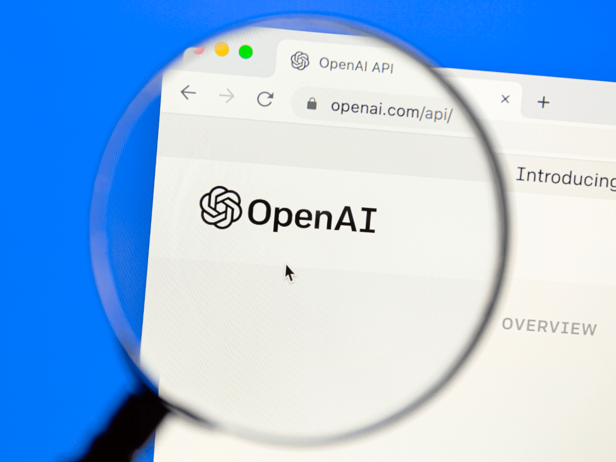A magnifying glass hovering over an OpenAI logo on an open laptop.