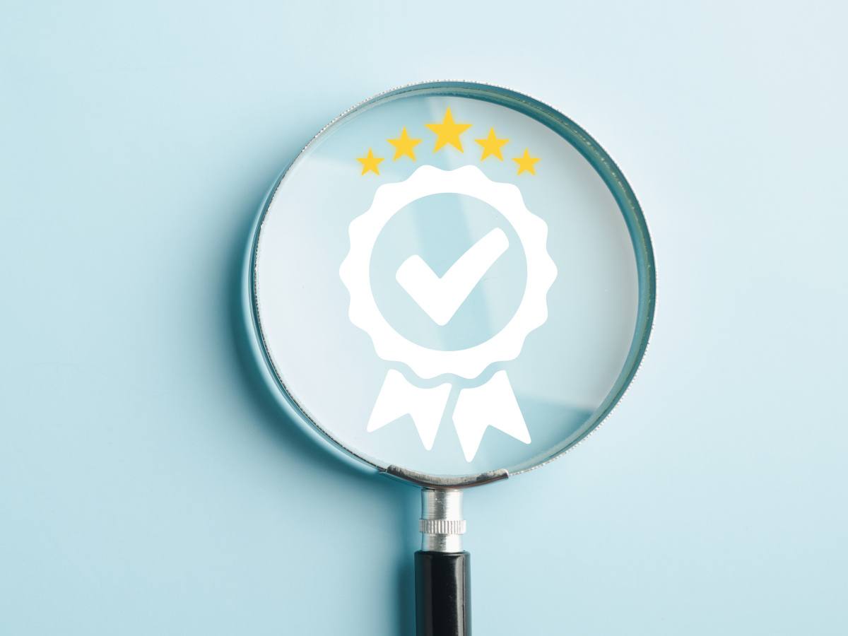 A picture of a magnifying glass held over a certification symbol on a blue board.
