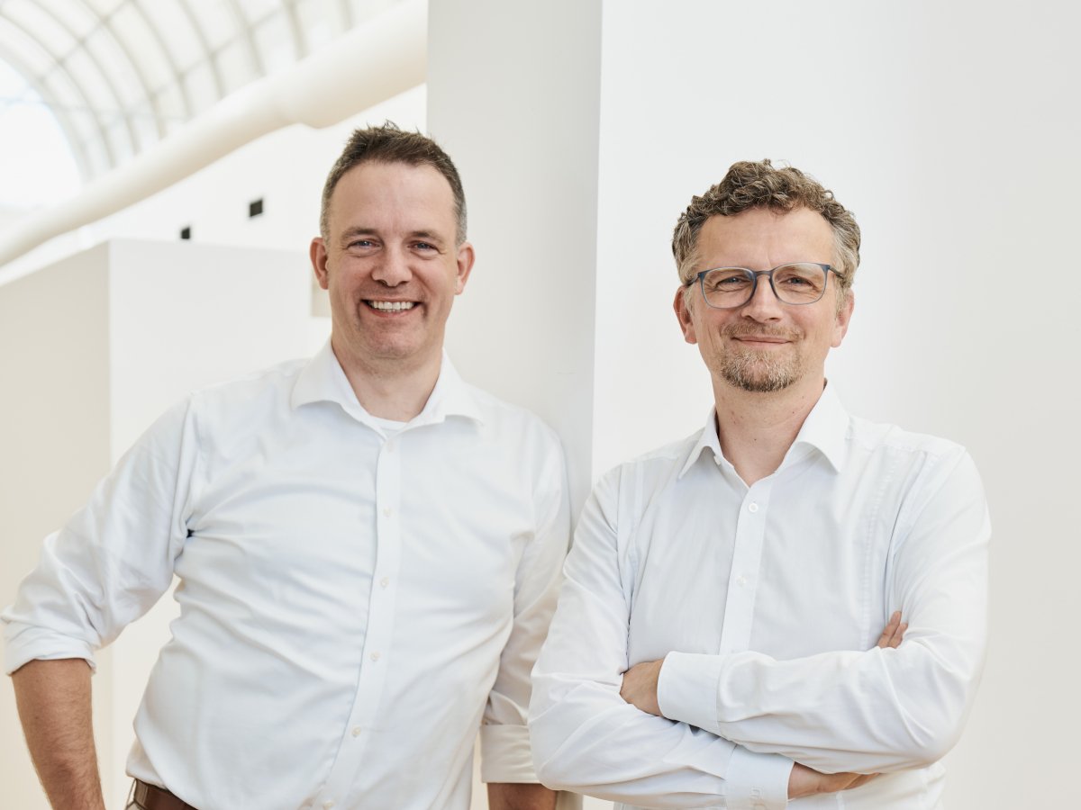 Two white men in white collared shirts smiling for the camera.