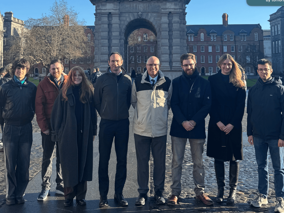 Team members from Trinity College Dublin posing in front of a large stone arch.
