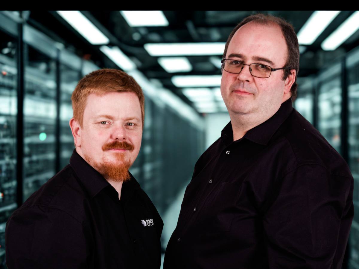 Two men in black shirts with their face tilted to the camera.