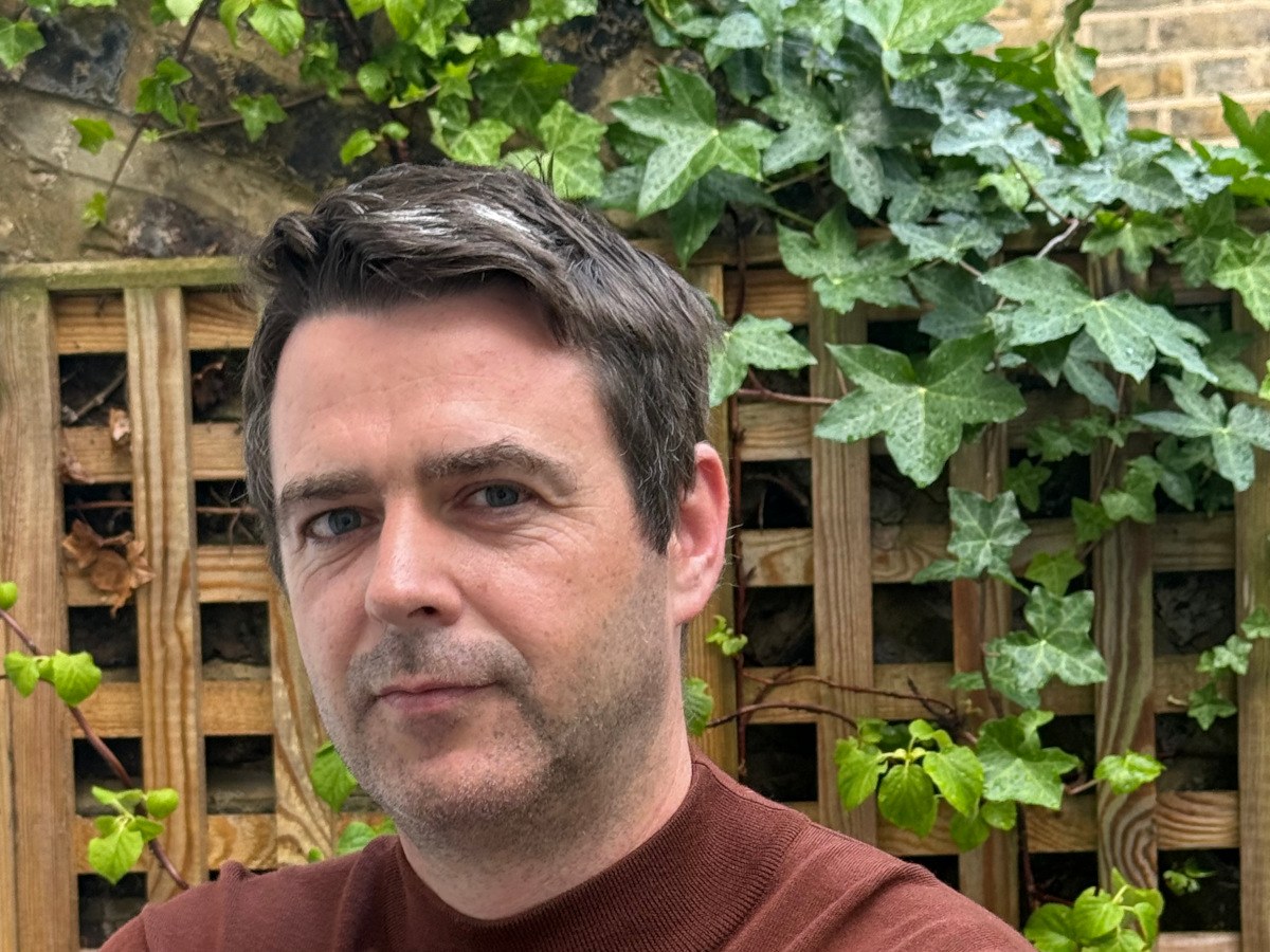 A middle-aged white man in a burgundy jumper, posing in a garden.