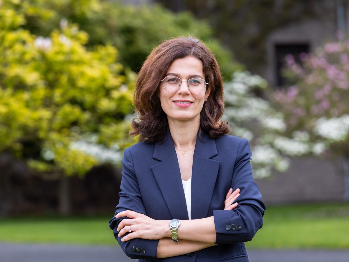 A person with voluminous shoulder length brown hair with a dark blue blazer.