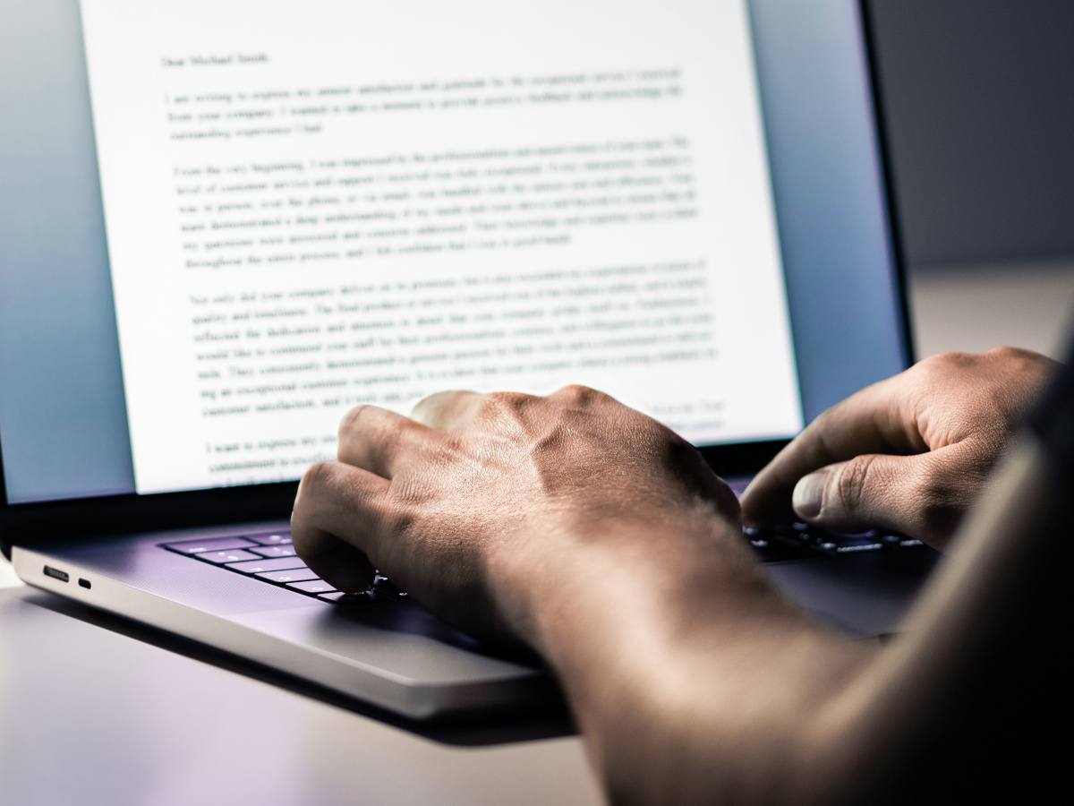 Hands typing into a laptop, a document on the screen filled with paragraphs of text.