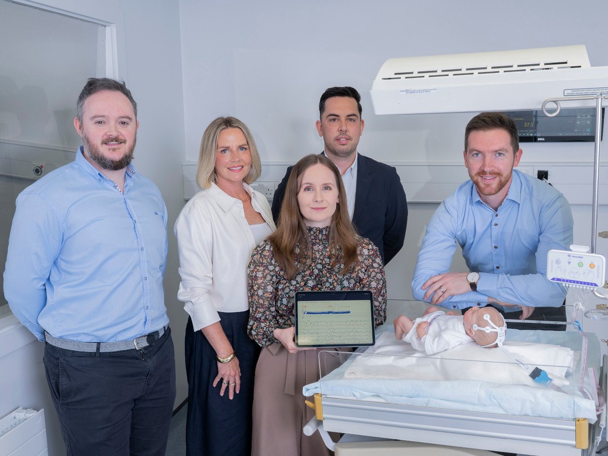 Three men and two women standing around a neonatal bed with a newborn baby doll.