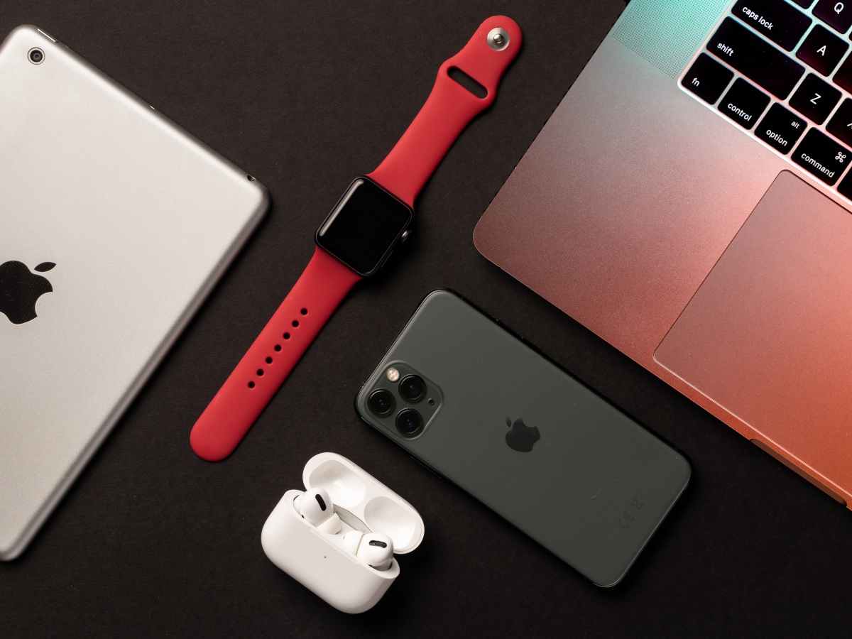 A picture of various Apple devices, including the iPhone, Apple Watch, iMac and AirPods, sitting on a dark grey surface.
