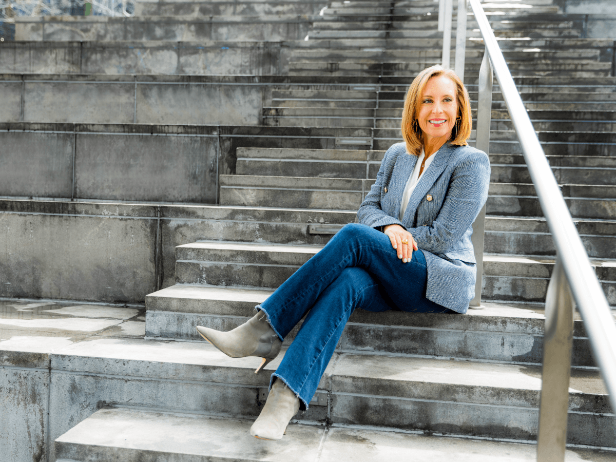 A middle aged white woman sitting on a stone step in a sports arena.
