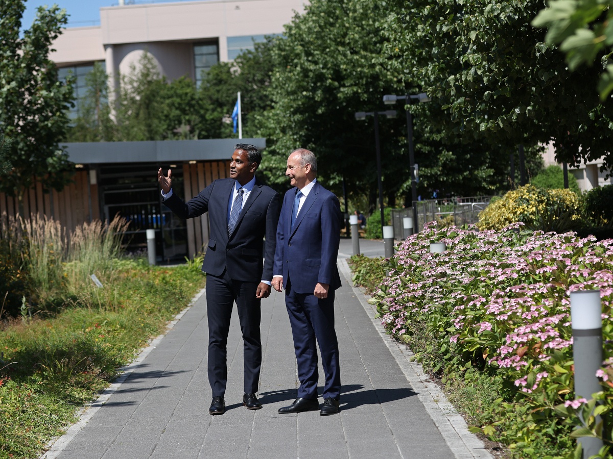 A white man and an Asian man in suits and ties stand on a pathway through a leafy campus at Intel in Leixlip, Kildare.