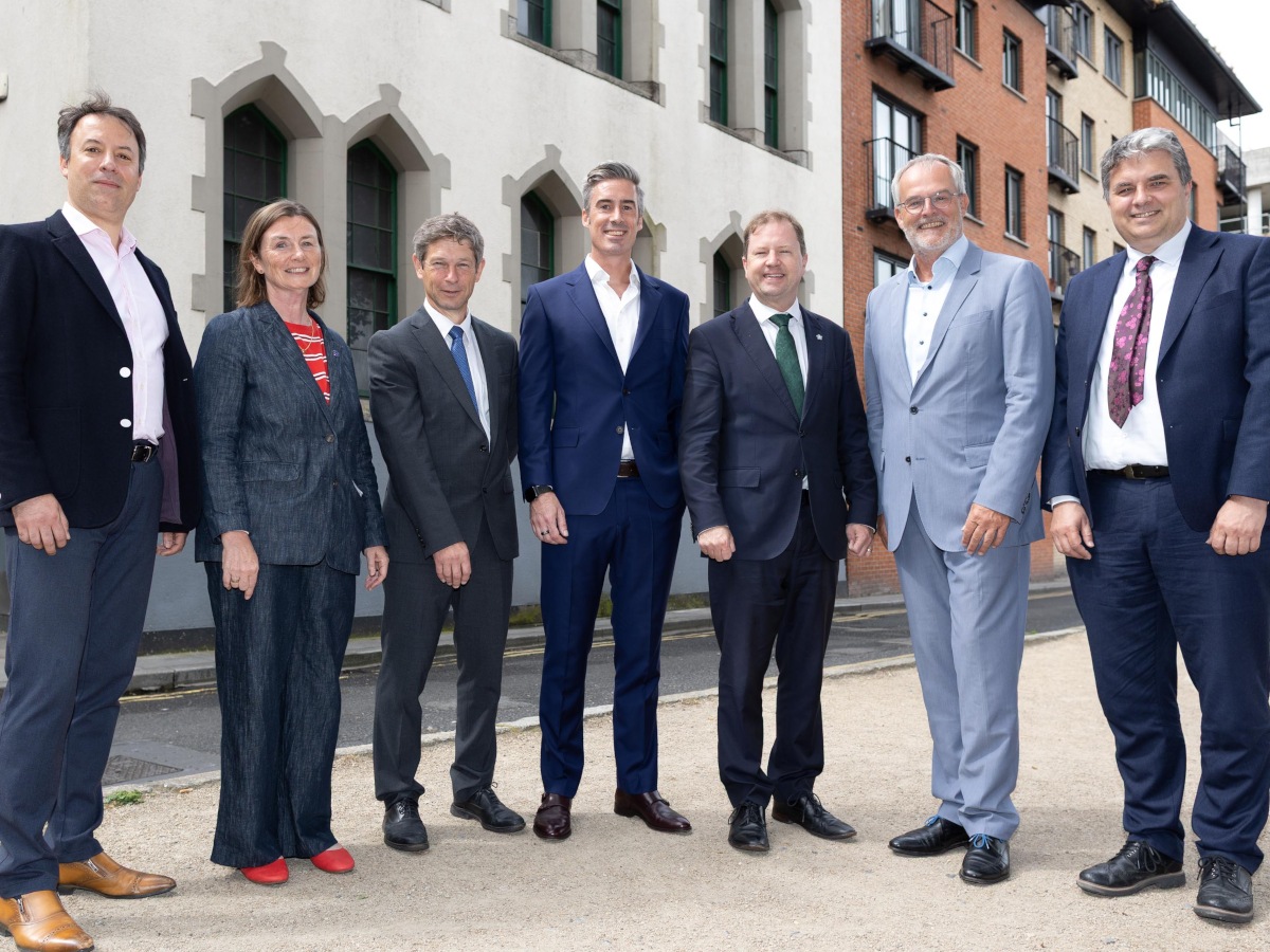 Six men and one woman in business clothing stand in a line, looking at the camera, on a city street.