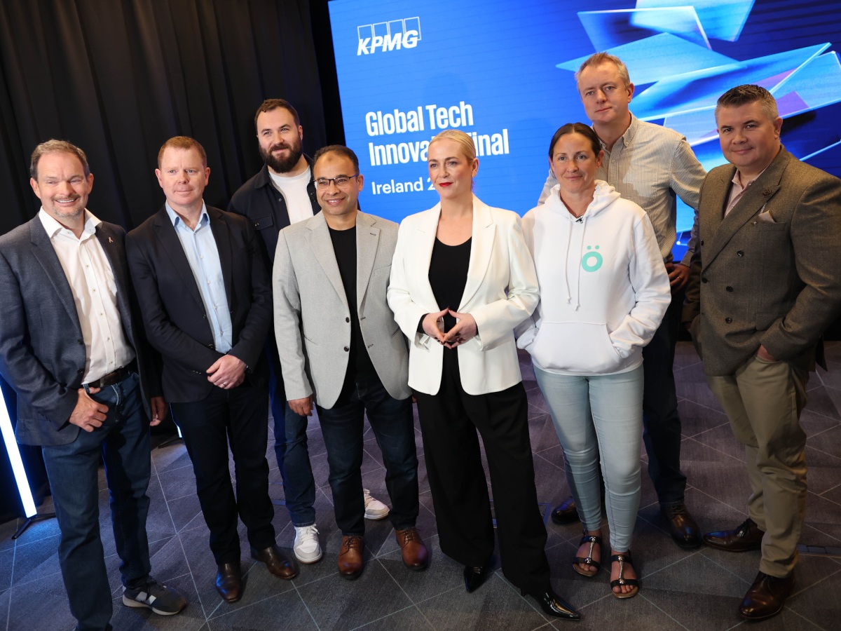 Six men and two women stand in a row in front of a blue KPMG Global Tech Innovator wall.