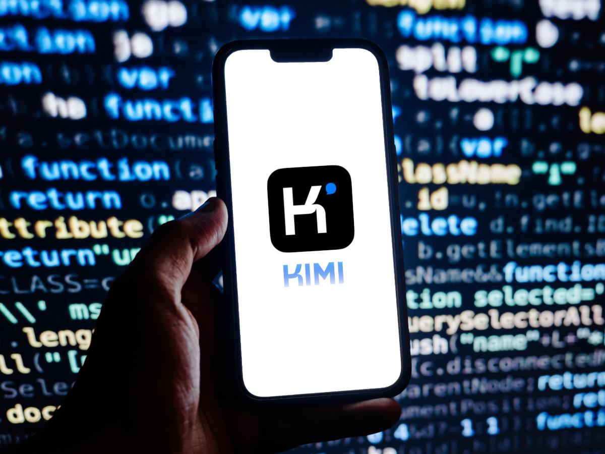 Kimi K2 Thinking logo on a phone against a screen with binary code.