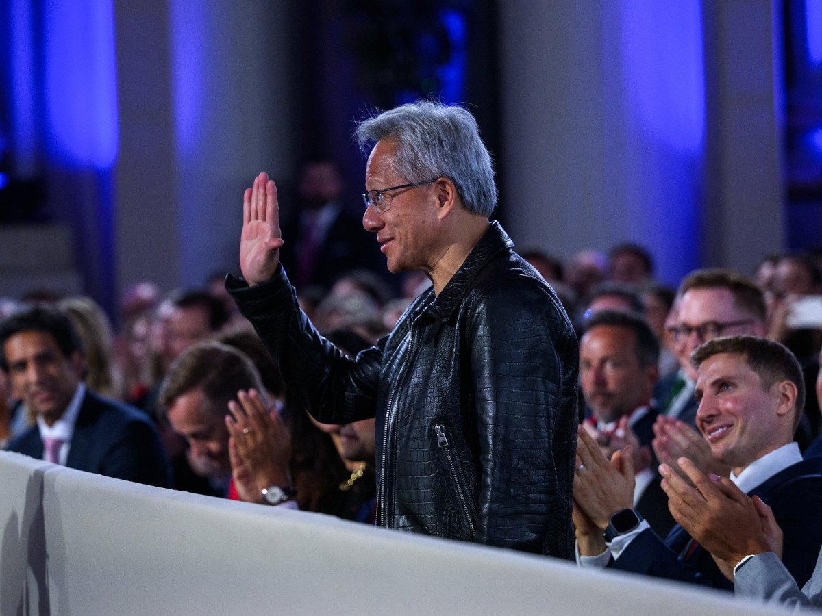 A man with grey hair and a leather jacket waving at someone outside of the frame. There