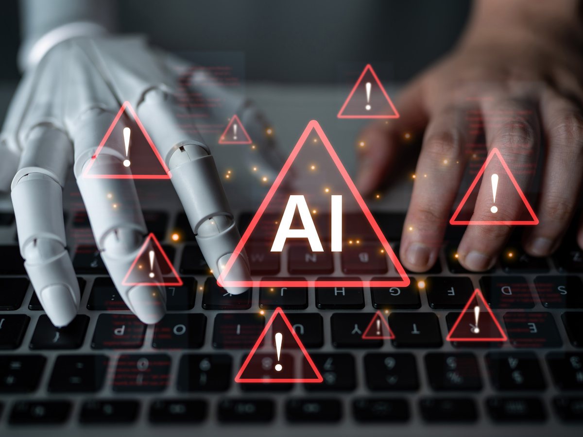 Two hands, one AI and one human, work on a laptop, with AI warning signs over the image.
